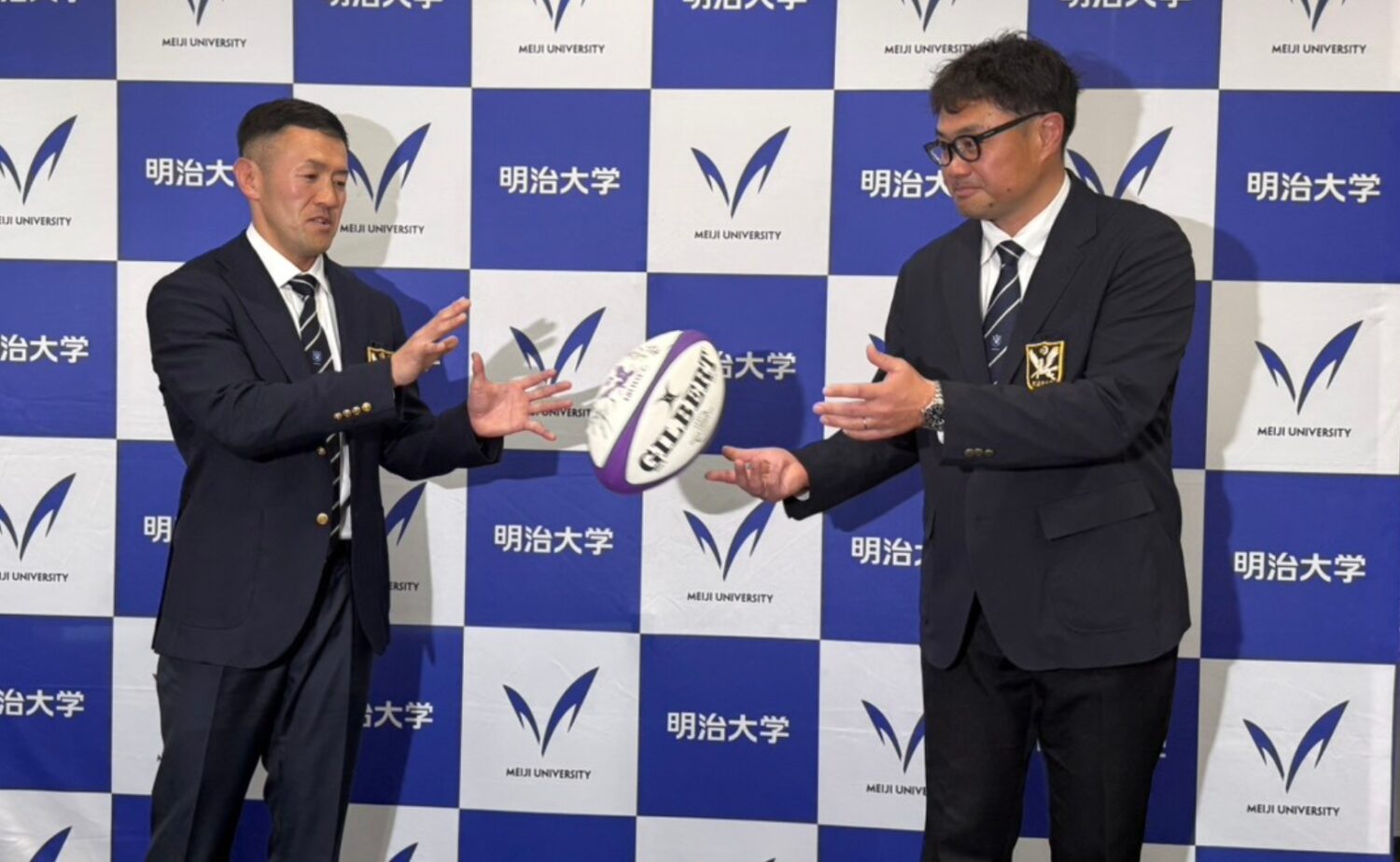 明治大学ラグビー部高野新監督(左)へパスを投げる神鳥監督