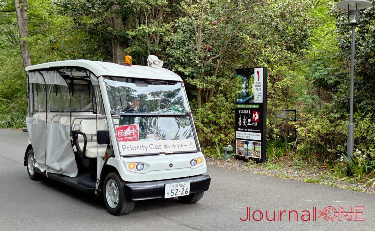 ムーミンバレーパーク内を走行する「おもいやりカー(Priority Car)」。豊かな緑を背景に、白い電動のオープン車両が路面を走る様子。