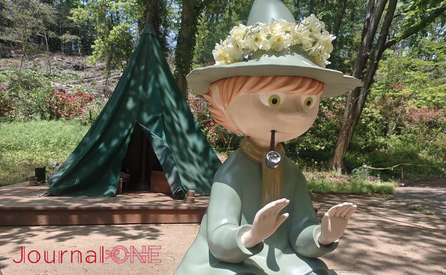 埼玉県飯能市のムーミンバレーパークにあるスナフキンのテント。手前には、黄色い花冠を帽子に乗せ、パイプをくわえて焚き火に手をかざすスナフキンの像が置かれている。