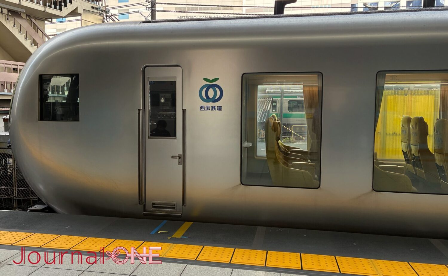 池袋駅のホームに停車する特急ラビュー（Laview）の外装。風景を柔らかく映し出すシルバーの流線型車体と、足元近くまで広がる大きな客室窓、西武鉄道のロゴマークが配置された近未来的なデザイン。