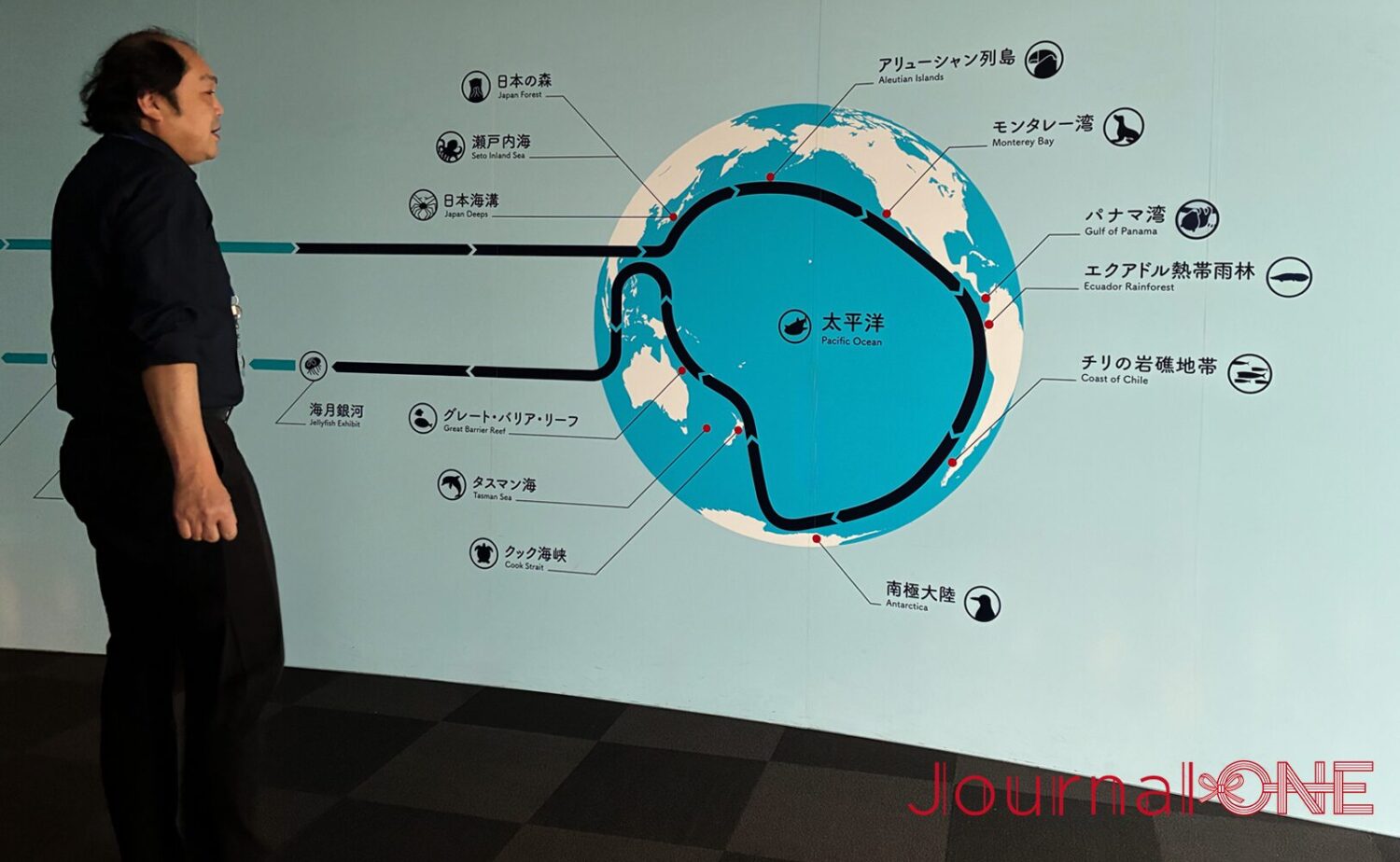 海遊館の展示ルートを示す館内マップの前に立つ田井さん。太平洋を中心に世界の海を巡る展示構成が紹介されている。