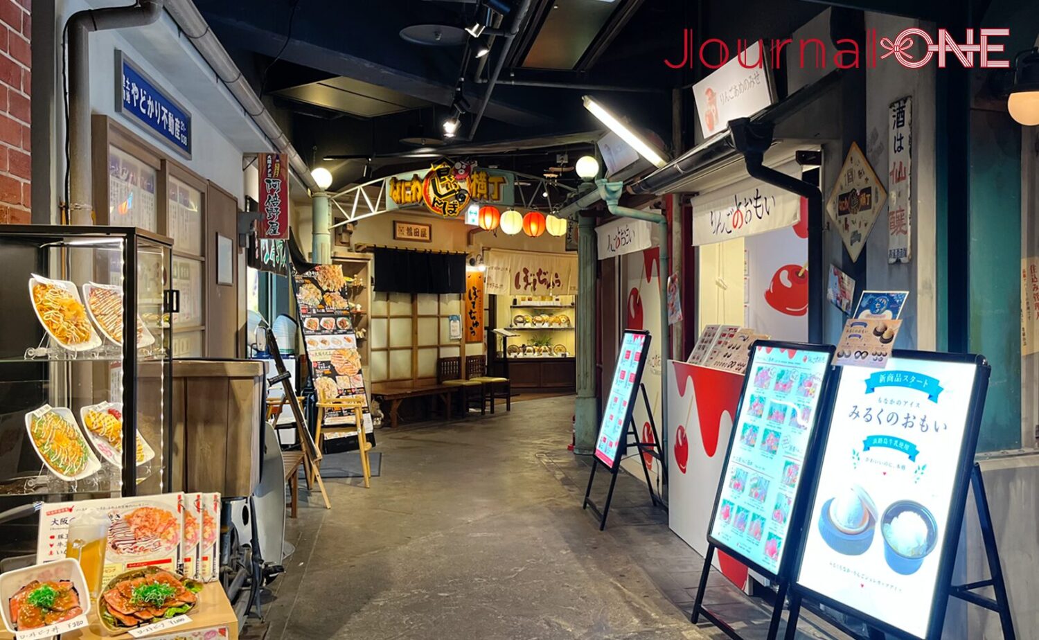 昭和30年代の大阪の下町を再現したフードテーマパーク「なにわ食いしんぼ横丁」のレトロな路地景観。手前左側にはたこ焼きやお好み焼きの食品サンプルが並ぶショーケース、右側には「りんごおもい」の看板や「みるくのおもい」のメニューボードを掲げたモダンな和菓子店が配され、奥へと続く通路には「なにわ食いしんぼ横丁」のアーチ看板や赤白の提灯、暖簾を掲げた飲食店が連なっている。