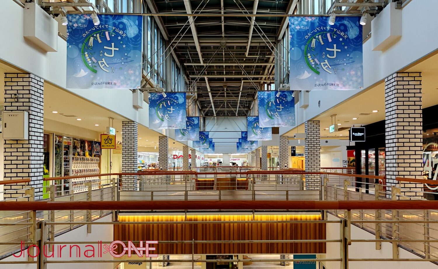 天保山マーケットプレイス2階のショッピングモール通路。高い天井へと続く開放的なアトリウム構造の下、白レンガ調の柱や木目調の手すりが並び、天井の梁からは七夕イベントを告知する青いフラッグが等間隔で複数吊り下げられている。