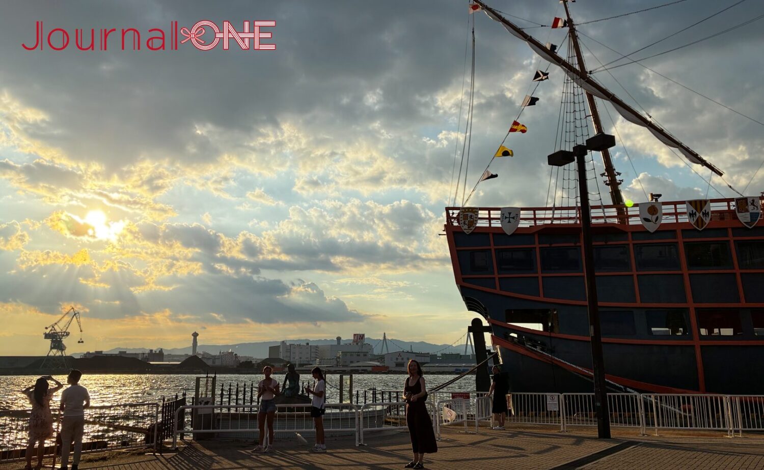 天保山の岸辺から望む夕暮れの大阪港。停泊するサンタマリア号の向こうに、夕日に照らされた海と港の景色が広がる。