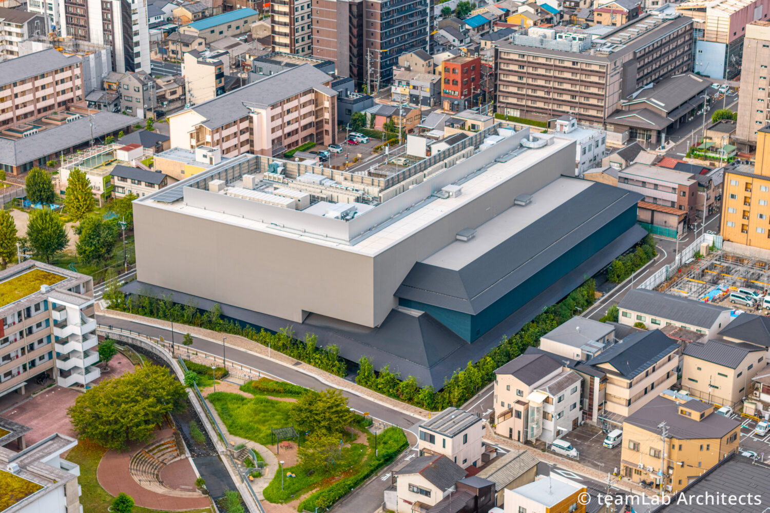 京都駅周辺に位置する常設展の拠点「チームラボ バイオヴォルテックス 京都」の建物外観を斜め上空から見下ろした鳥瞰カット。延べ面積約1万平方メートルを誇る国内最大規模の常設型ミュージアムである。