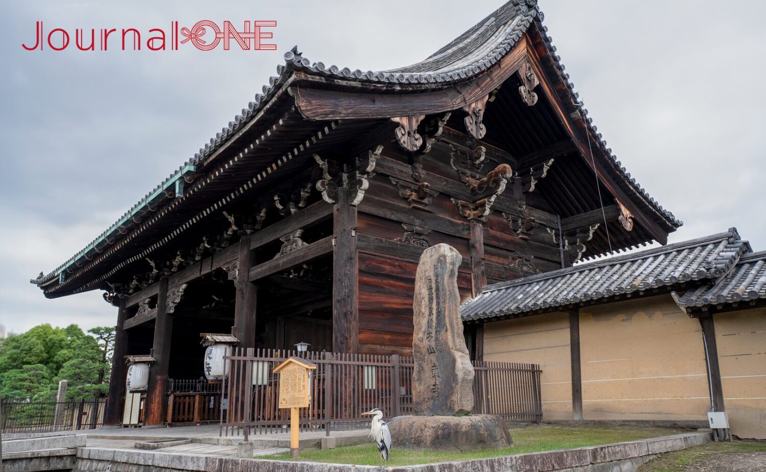 京都府京都市南区に位置する世界遺産「東寺（教王護国寺）」の重要文化財である「南大門」の全景。八脚門様式の重厚な木造建築と本瓦葺きの大きな屋根が佇み、手前には「真言宗総本山 東寺」と刻まれた石碑と築地塀、立て札や提灯が配置されている。