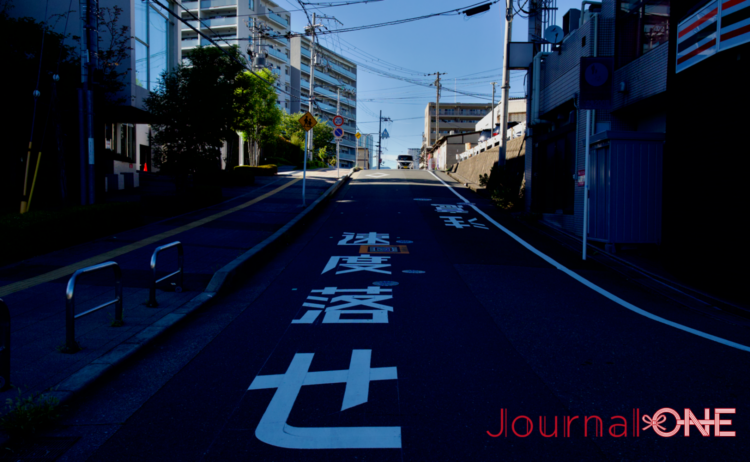 千里ニュータウンの竹見台マーケットへ続く坂道。尾根筋に広がる住宅地には「速度落とせ」の路面標示が描かれている。