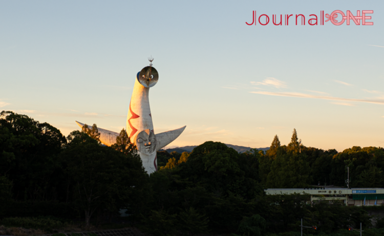 夕陽に照らされた太陽の塔。万博記念公園の深い緑の向こうに白い塔が浮かび上がる。