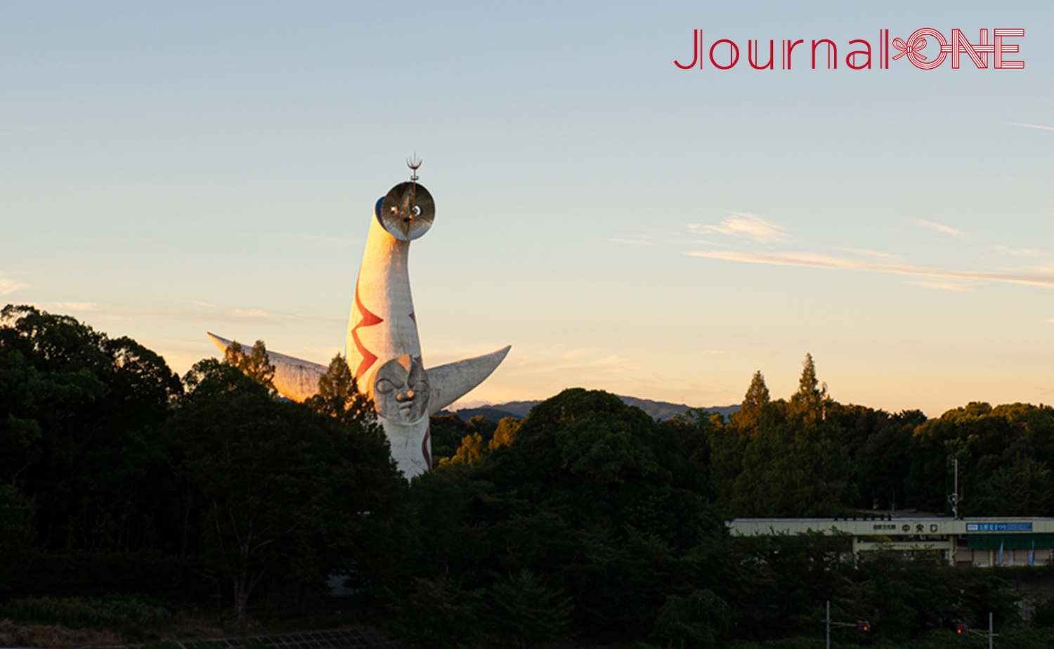 夕陽に照らされた太陽の塔。万博記念公園の深い緑の向こうに白い塔が浮かび上がる。